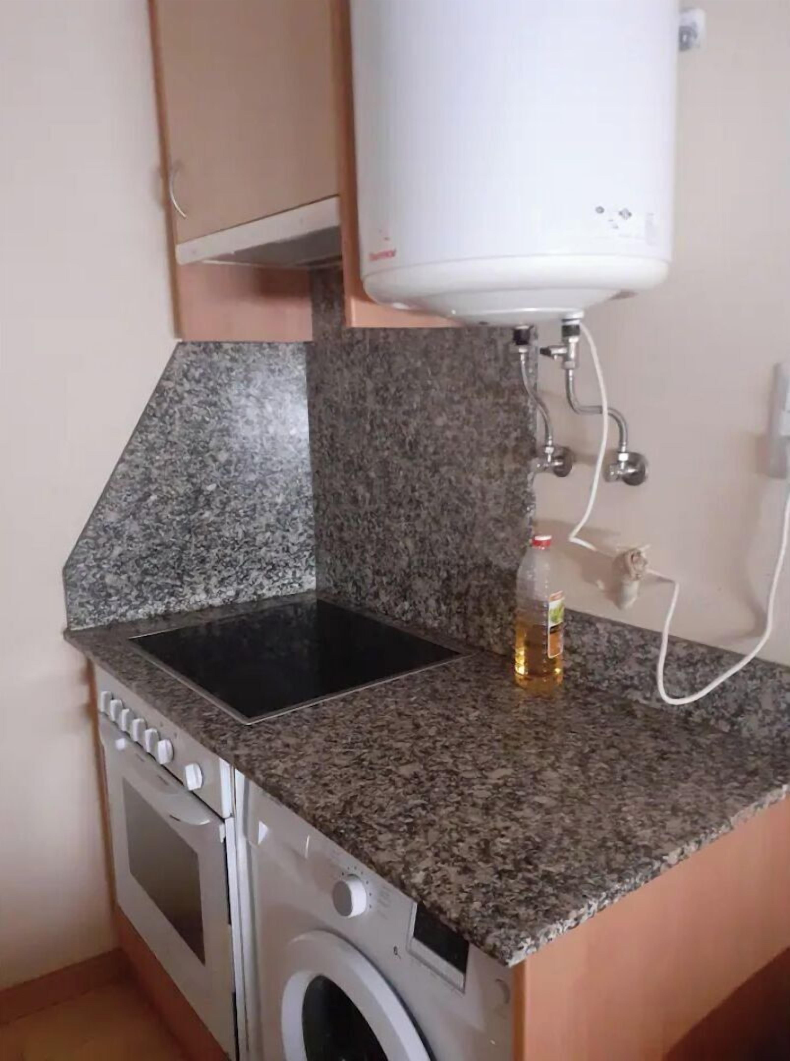 Una cocina con encimeras de granito, estufa, lavadora y calentador de agua.