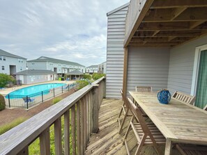 Une terrasse en bois avec une piscine, des chaises longues et une table agrémentée d’un vase bleu.