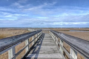 A wooden boardwalk extending into the distance with a clear sky above. - Turtle Cove 134 | Private Community Pool and Beach Access (Surf City)