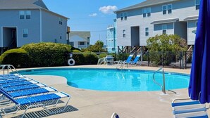 A swimming pool with blue lounge chairs, a small slide, and a fenced area with a blue umbrella. - Turtle Cove 134 | Private Community Pool and Beach Access (Surf City)