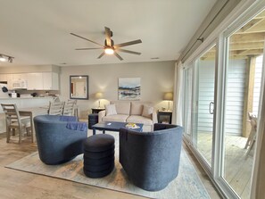 A modern living room with a ceiling fan, a dining area with a table and chairs, and a large sliding glass door leading to an outdoor area.