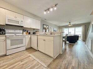 Une cuisine moderne avec des meubles blancs, un four à micro-ondes encastré et un grand îlot central doté d’un évier.