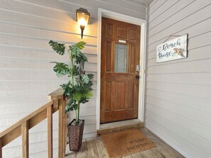 A wooden door with a glass panel, a potted plant, a welcome mat, and a sign reading 'Beach House'.