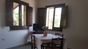 A dining area with a table set for four, a television on a stand, and a window with wooden shutters.