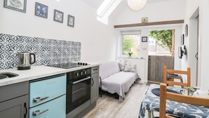 A compact kitchen with a built-in oven, a coffee maker, and a dining area with a table and chairs. - Little Crabapple (Swanage)