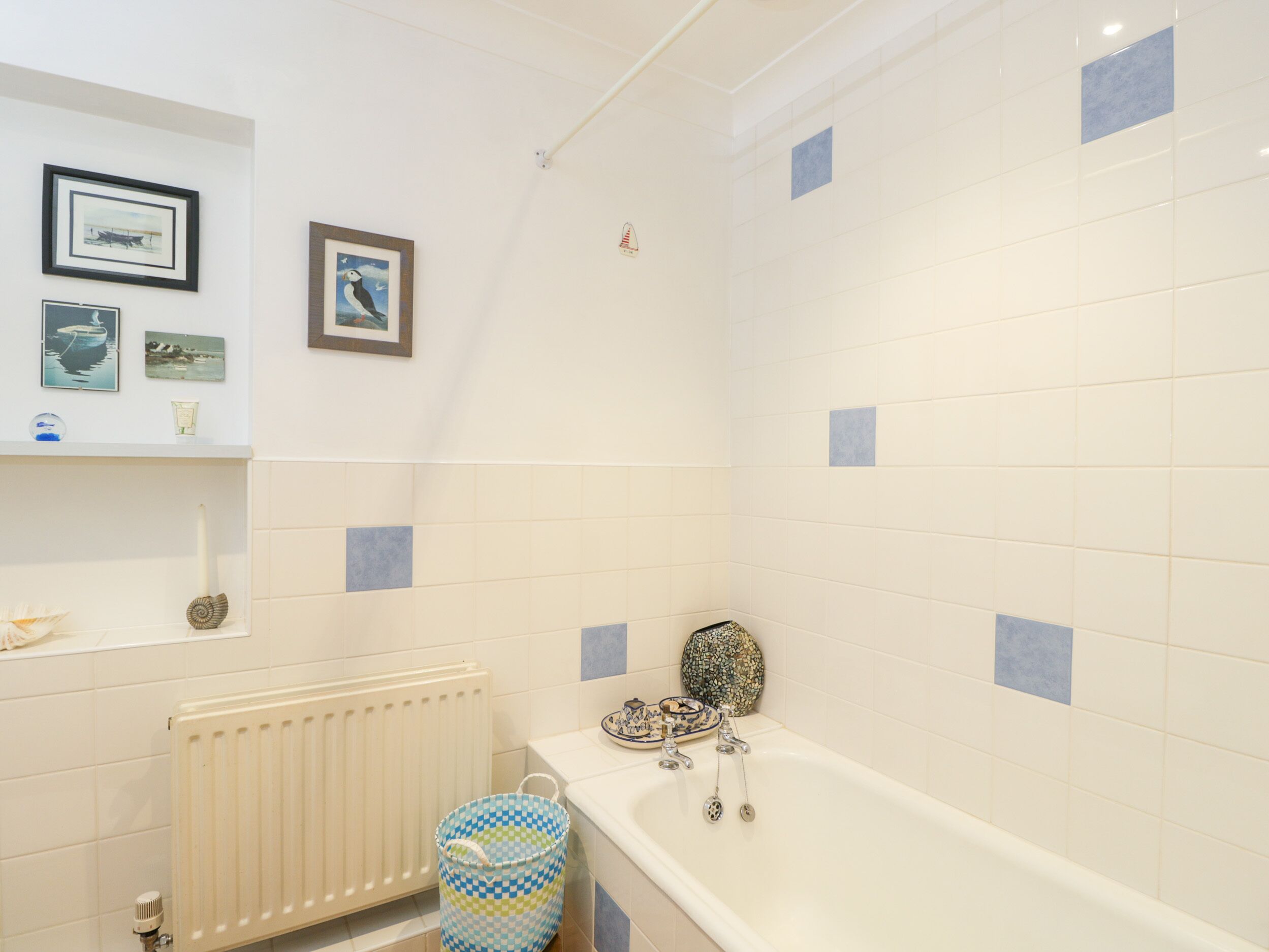 A bathroom with a bathtub, a toilet, and a radiator. There are framed pictures on the wall and a small shelf with decorative items.