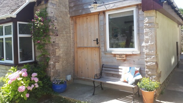 A small stone cottage with a wooden door, a bench outside, and potted plants. - Little Crabapple (Swanage)
