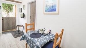 A dining area with a table set for two, a wooden chair, a framed picture on the wall, and a door leading outside. - Little Crabapple (Swanage)