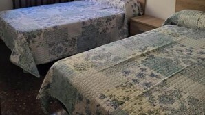 Een kamer met twee eenpersoonsbedden, een houten hoofdbord, een nachtkastje en een raam met gordijnen.