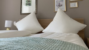 Ein ordentlich bezogenes Bett mit weißen Kissen und einer grünen Decke, eine Nachttischlampe und gerahmte Bilder an der Wand.