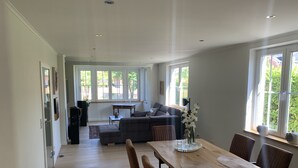 Ein geräumiger Wohnbereich mit Esstisch, Sofas und Blick ins Freie durch große Fenster.