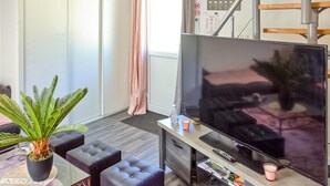A modern living room with a flat-screen TV, a potted plant, and a sofa.