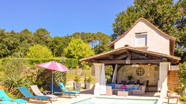 A poolside area with lounge chairs and a covered seating area with cushions.