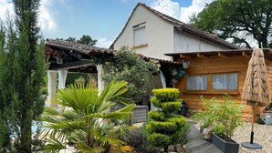 A house with a wooden exterior, a tiled roof, and a garden with various plants and a wooden deck.