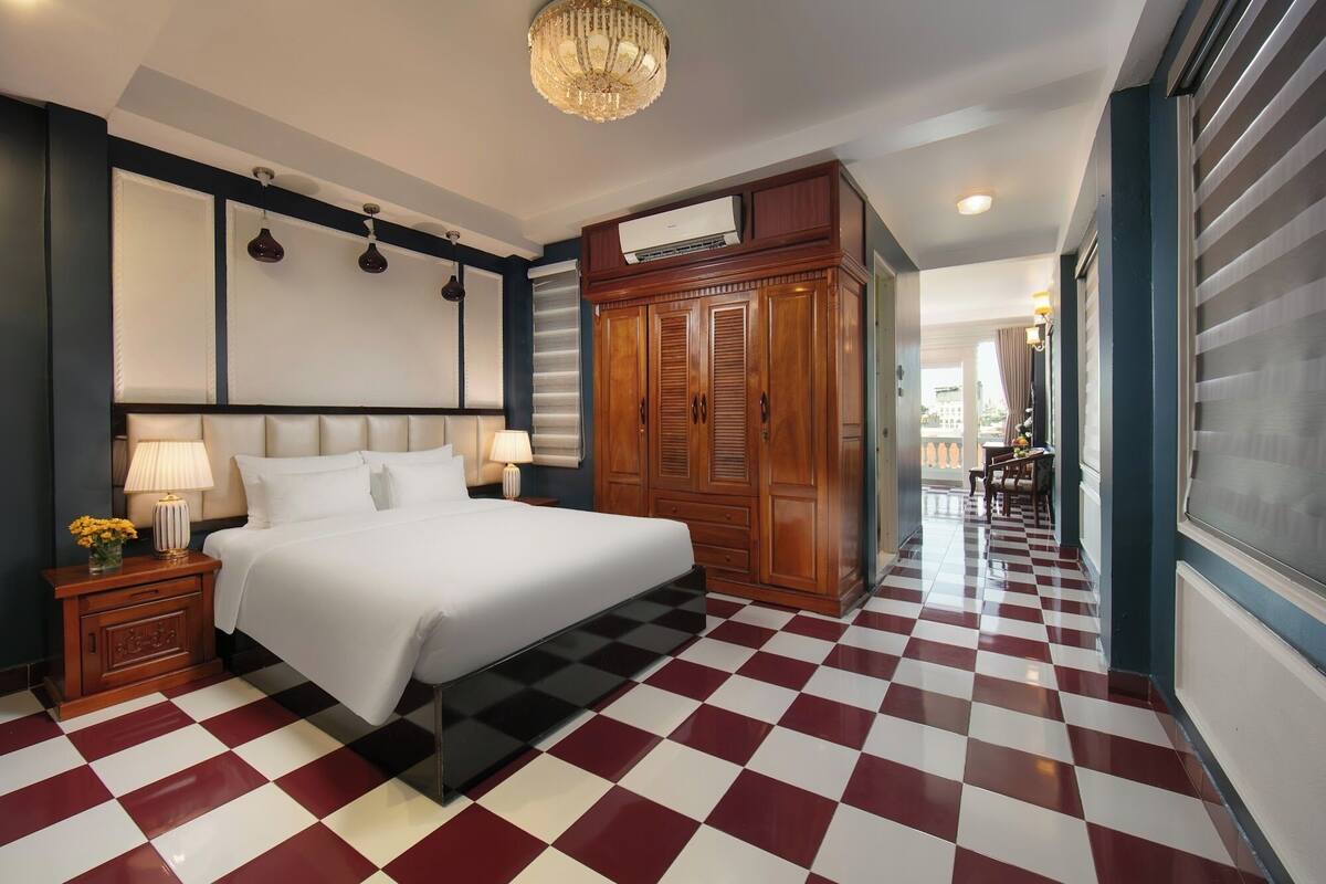 A hotel room with a checkered floor, a large bed, a wooden wardrobe, and a chandelier.