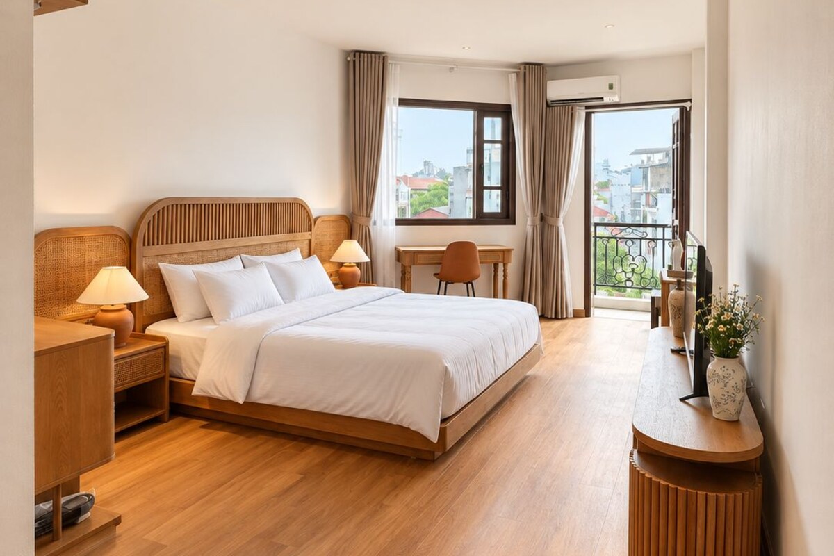 A hotel room with a large bed, a desk, a chair, a small table, and a balcony with a view.