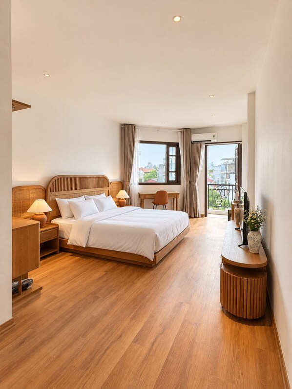 A hotel room with a large bed, a desk, a chair, a small table, and a balcony with a view. - Hanoi Delica Hotel (Hanoi)
