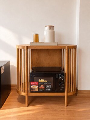 A kitchen area with a microwave on a wooden stand, a white vase, and a black refrigerator. - Hanoi Delica Hotel (Hanoi)