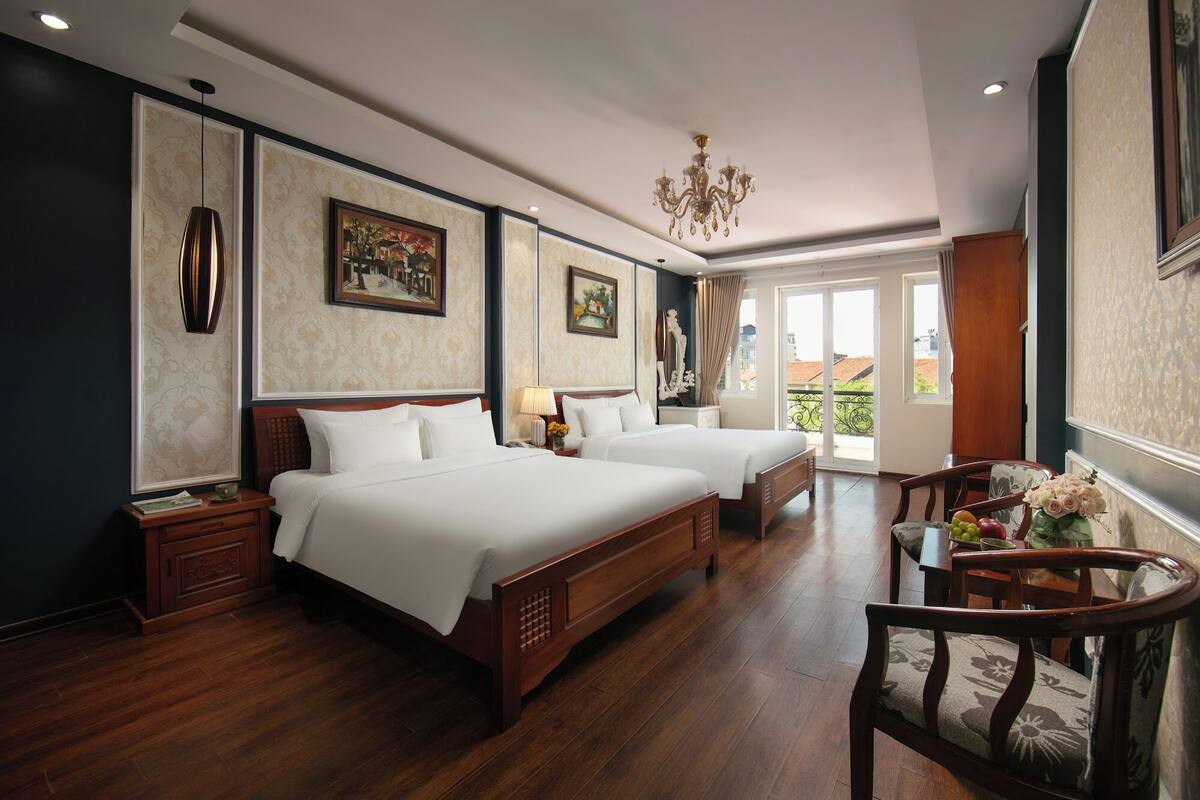 A hotel room with two beds, a chandelier, and a dining area with a table and chairs.