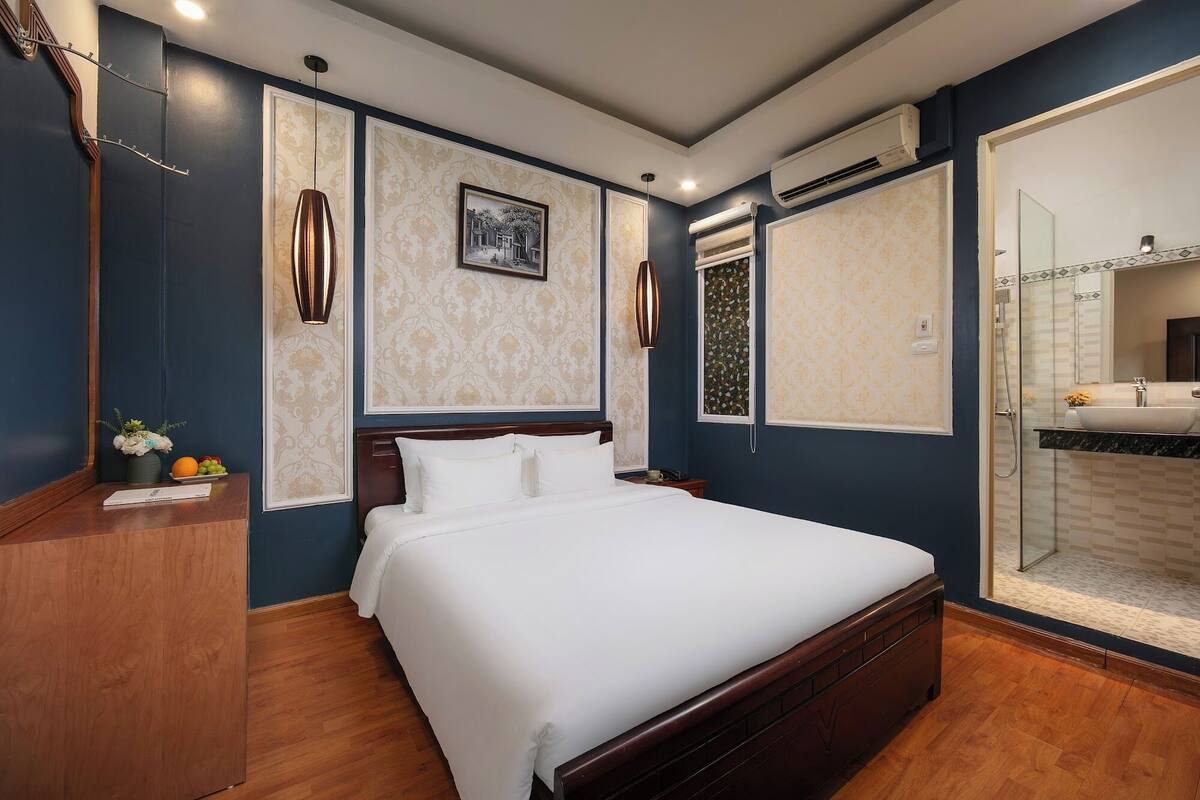 A hotel room with a bed, a vanity with a mirror, and a shower area.