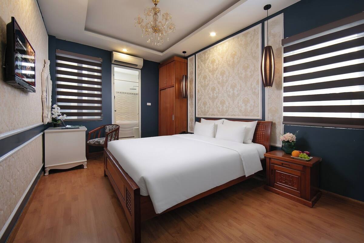 A bedroom with a large bed, wooden wardrobe, bedside table with fruit, and a TV on the wall.