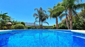 A clear blue pool surrounded by lush greenery and palm trees, with a mountain in the background. - Quiet Villa with heated swimming pool, barbecue and views. (Alhaurín el Grande)