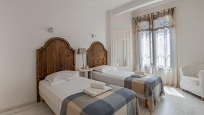 Ein Zimmer mit zwei Betten, einem kleinen Tisch mit einer Lampe, einem Stuhl und einem Fenster mit Vorhängen.