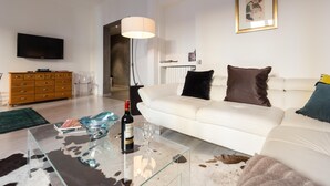 Ein modernes Wohnzimmer mit einem weißen Sofa, einem Glastisch, einem Fernseher und einer Lampe.