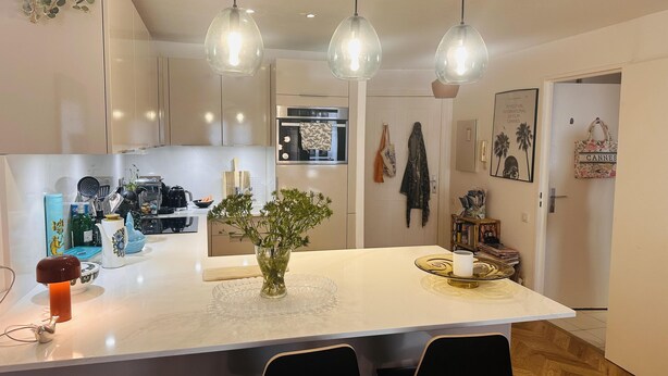 A modern kitchen with a central island, pendant lighting, and a view into the dining area.