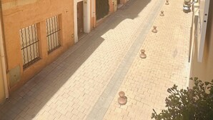 A narrow street with buildings on either side, featuring traditional architecture with shutters and balconies.