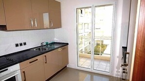 Una cocina con armarios color beige, encimera negra y puerta corrediza de vidrio que da a un balcón.