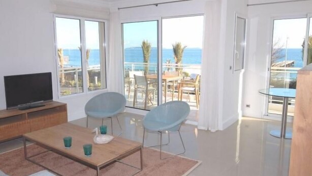 Una sala moderna con un televisor grande, dos sillas azules, una mesa de centro de madera y una mesa de comedor de vidrio.