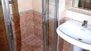 Ducha con cerramiento de vidrio, lavamanos blanco y espejo superior.