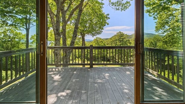 A wooden deck with a glass door leading to a forested area.