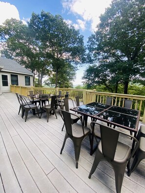Una terraza exterior con una mesa y sillas de vidrio, rodeada por otra terraza de madera y una barandilla amarilla.