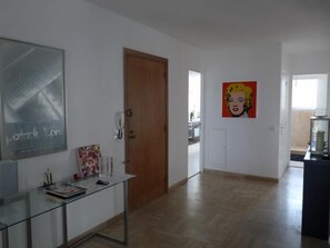 A spacious hallway with a wooden door, a glass table with a magazine, and a pop art painting on the wall.