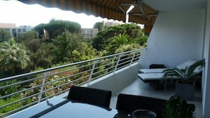 Un balcon avec une table et des chaises, une balustrade, et une vue sur un jardin luxuriant et des bâtiments.