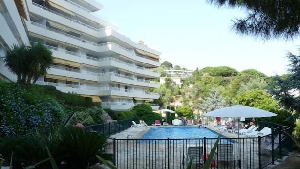 Un hôtel à plusieurs étages doté d’une piscine entourée de verdure et d’un espace clos aménagé avec des chaises longues.
