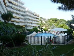 A multi-story hotel with a swimming pool surrounded by greenery and a fenced area with lounge chairs.
