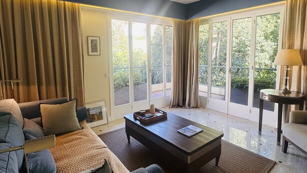 A spacious living room with a sofa, coffee table, and a view of a balcony with curtains.