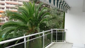 A balcony with a glass railing, a palm tree, and a view of a building in the background. - Three bedroom, two bathroom apartment in Cannes with large terrace - 880 (Cannes)