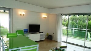 A modern living room with a dining area, a flat-screen TV, and a large window offering a view of greenery. - Three bedroom, two bathroom apartment in Cannes with large terrace - 880 (Cannes)