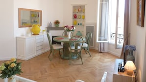 Ein Essbereich mit Holzboden im Fischgrätmuster, einem runden Tisch mit Stühlen, einem weißen Schrank und einem Fenster mit Vorhängen.
