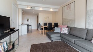 A modern living room with a grey sofa, a flat-screen TV, and a glass coffee table. - Modern 3BR/3BA cannes apt walk to Palais - 2000 (Cannes)