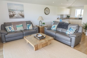 A living room with two grey sofas, a wooden coffee table, and a painting of a beach scene. - Sandpiper (Perranporth)