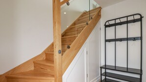 Una escalera de madera con barandilla de vidrio y un estante de metal negro en la pared.