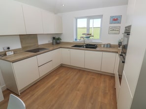 A modern kitchen with white cabinets, a wooden countertop, a sink, and a window with a view of the outdoors. - Sandpiper (Perranporth)