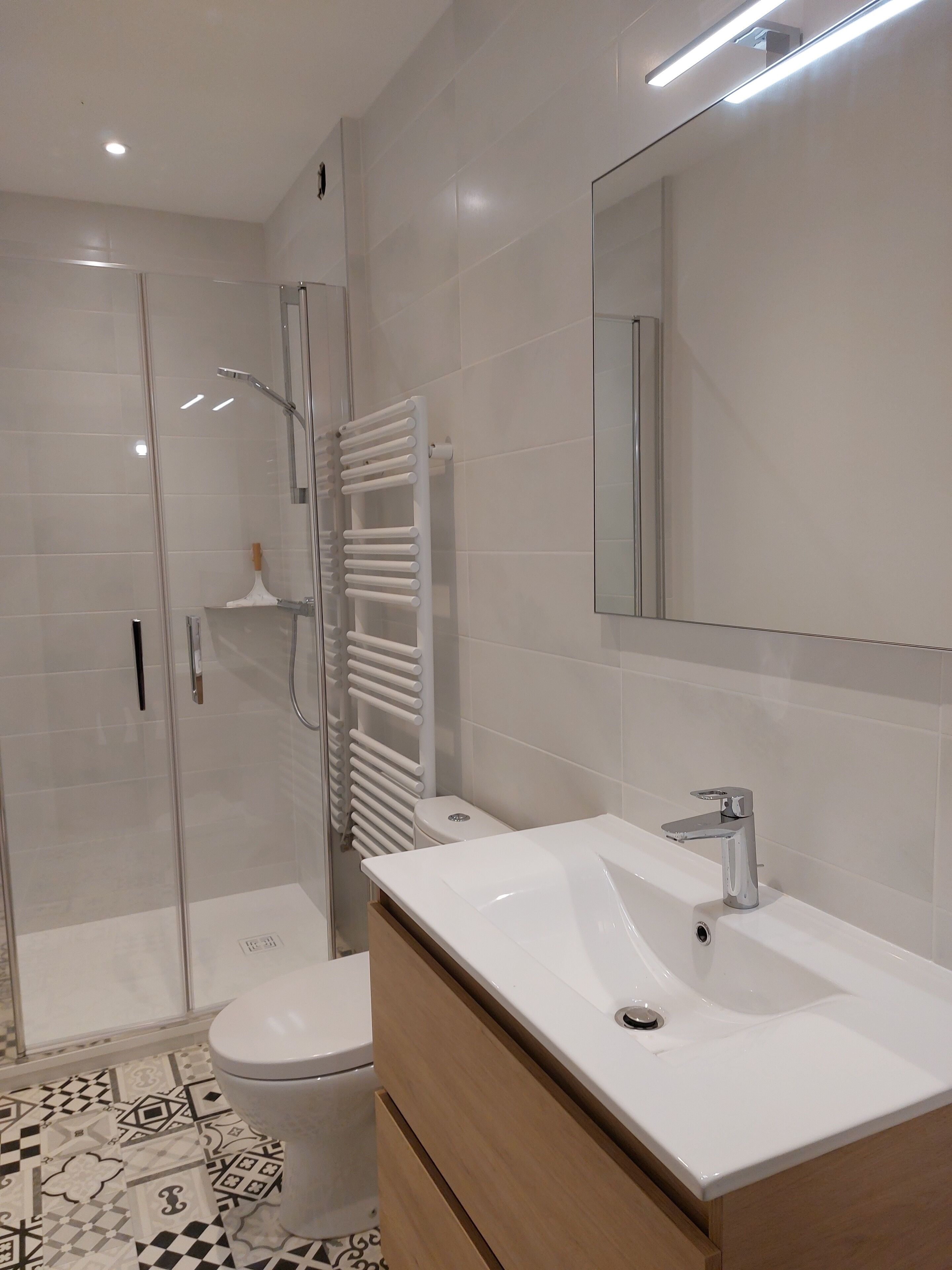 Ein modernes Badezimmer mit Duschkabine aus Glas, einer weißen Toilette, einem weißen Waschbecken mit Spiegel darüber und einem gestreiften Boden.