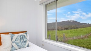 Ein Schlafzimmer mit großem Fenster und Blick auf ein grünes Feld und Hügel.