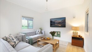 Ein geräumiges Wohnzimmer mit großem Fenster, einer Couch, einem Couchtisch und einem Gemälde an der Wand.